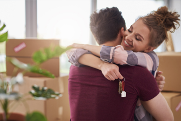 A man and a woman hugging and holding keys to their new home in front of moving boxes.