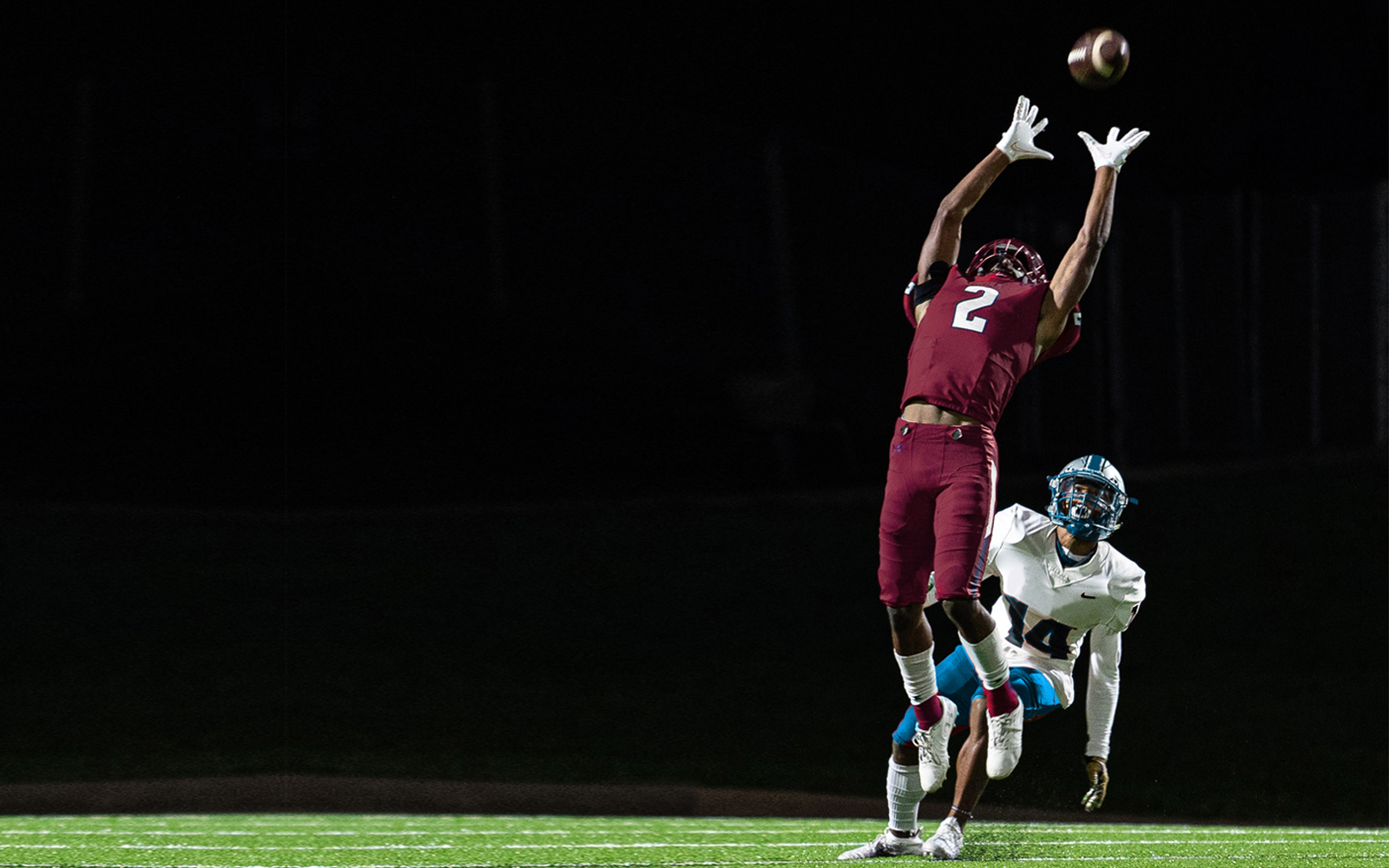 Two football players with one jumping up to catch the ball.