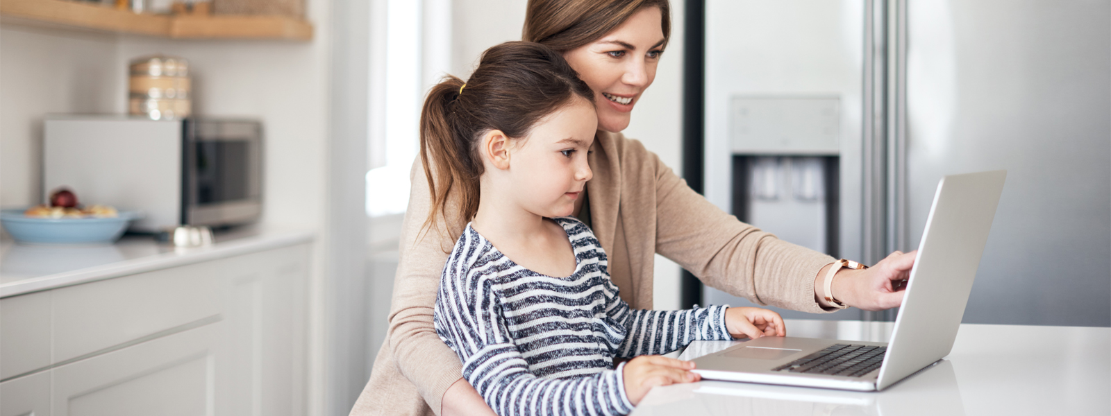 A woman and her daughter sitting in the kitchen looking at a laptop.