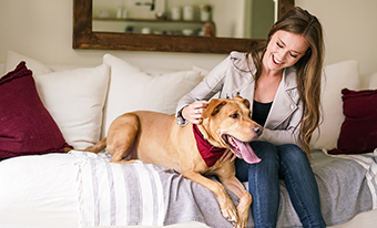 Female sits on couch with dog.