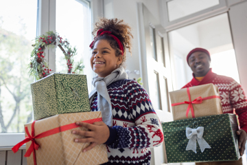 A man and a woman walking into a house holding gifts.