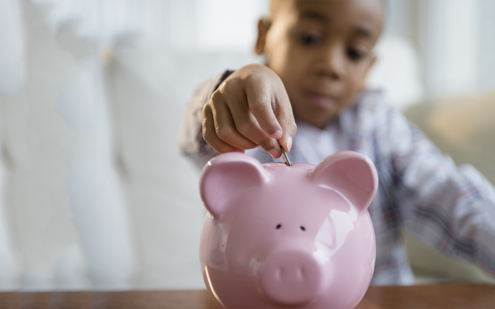 A young boy putting a coin into a piggy bank.