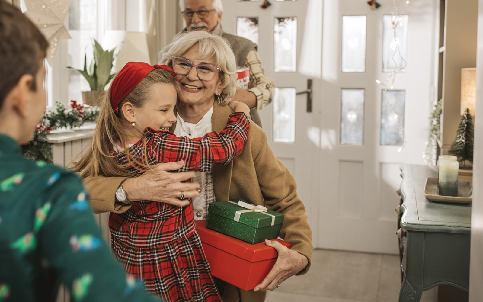 A young girl hugging her grandmother that is holding two presents.