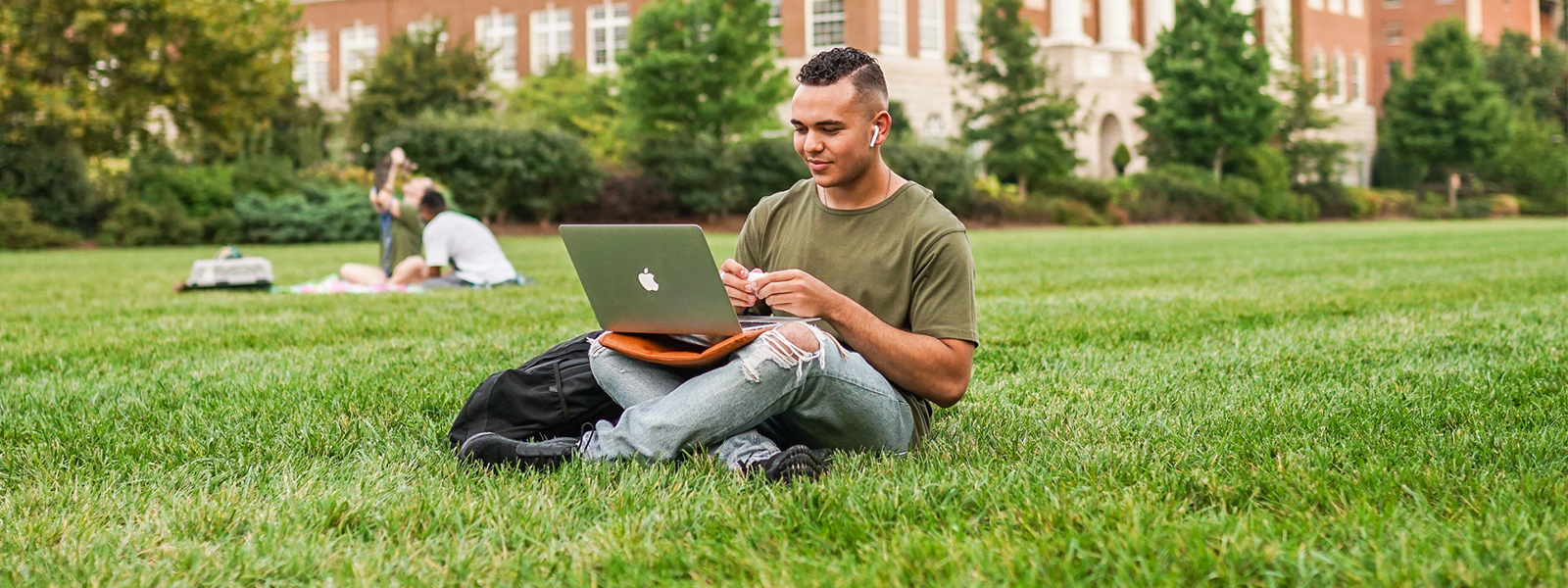 A student sits outside working on his computer