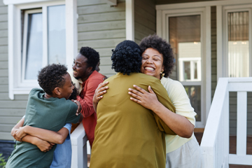 A group of people hugging outside a home.
