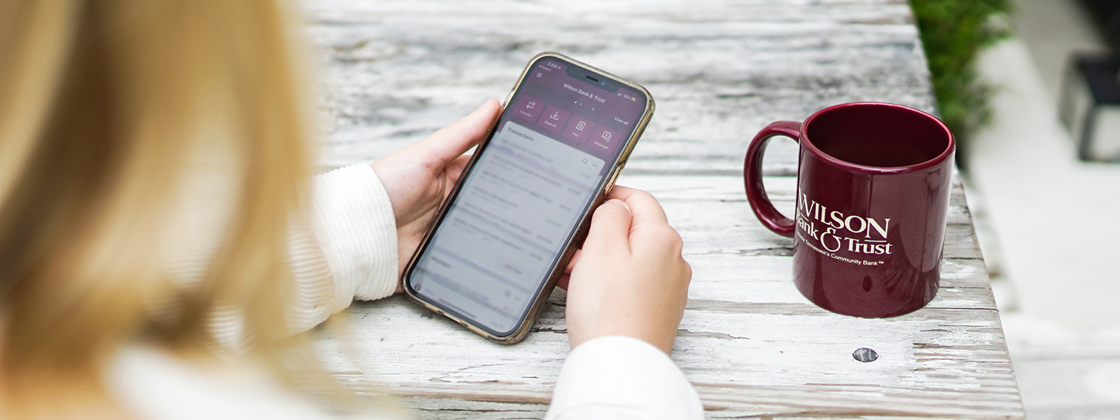 A woman looking at her bank app with a mug next to her.