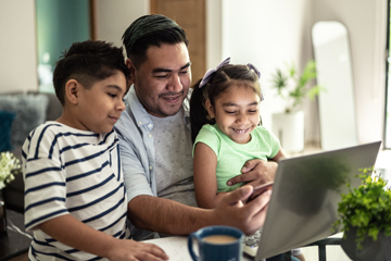 An image of a father with his young daughter and son looking at a laptop.
